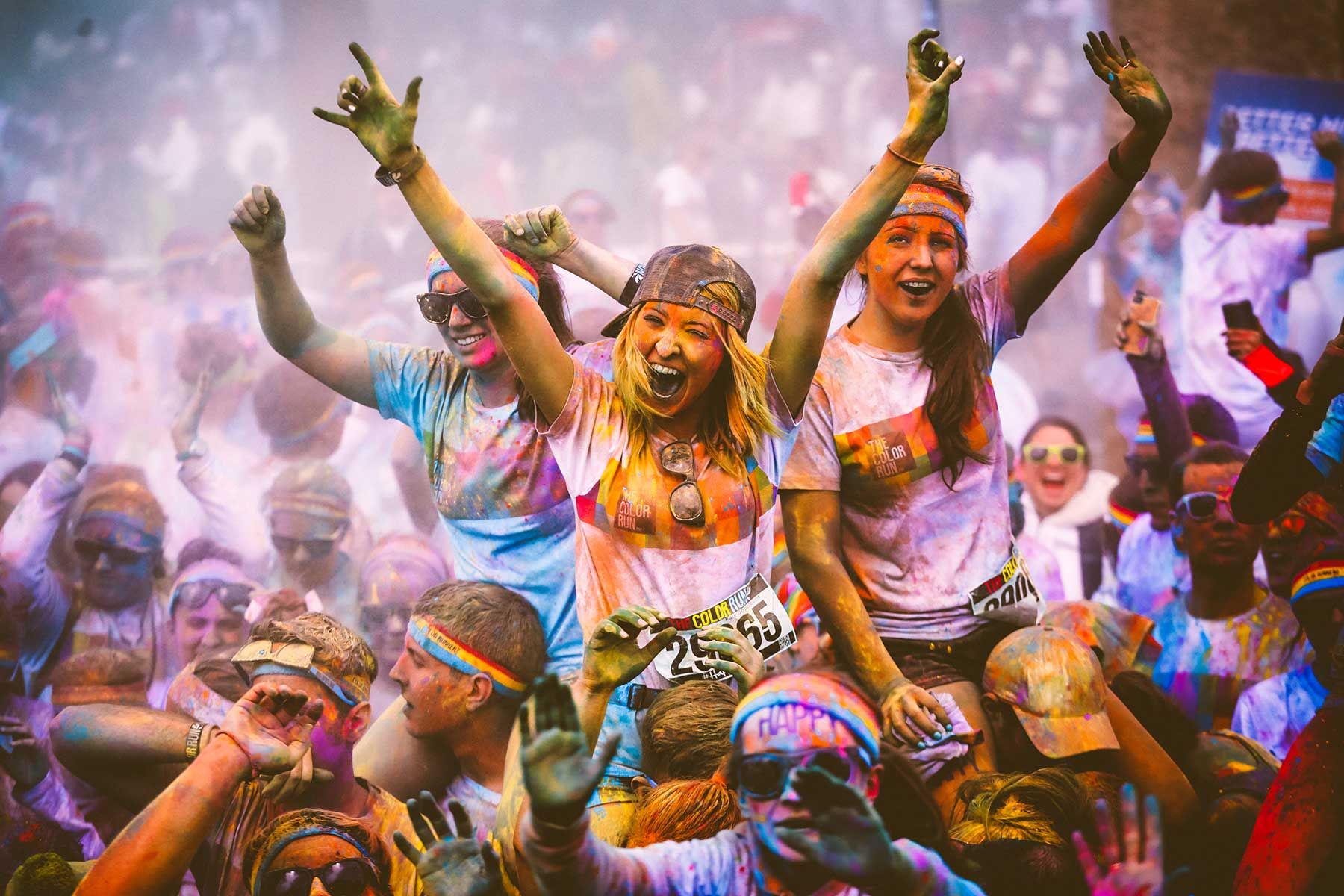 Color Run participants wearing branded event t-shirts and race bibs, covered in colored powder