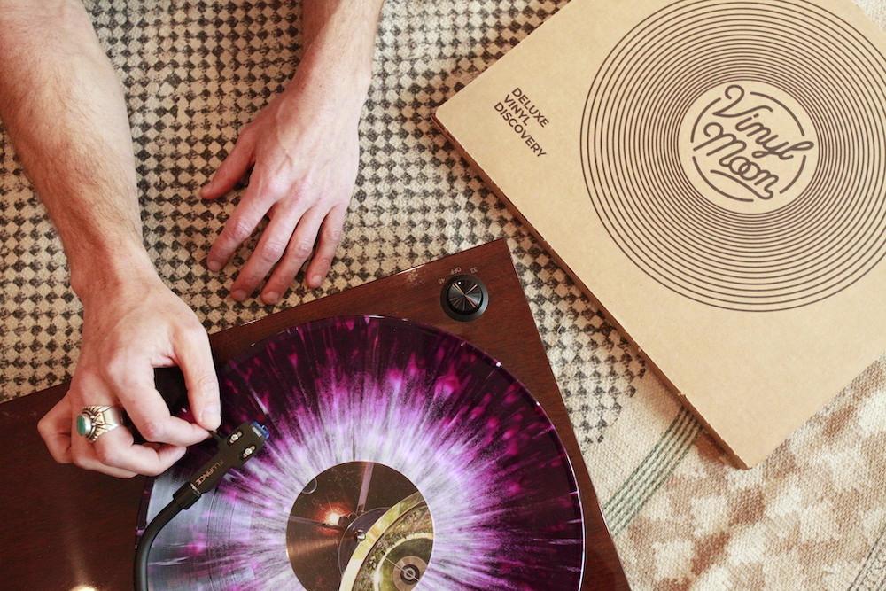 A Vinyl Moon record spinning on a turntable next to its Deluxe Vinyl Discovery box