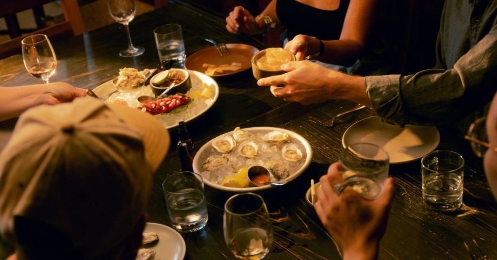 Friends sharing oysters, crudo and drinks around a candlelit restaurant table