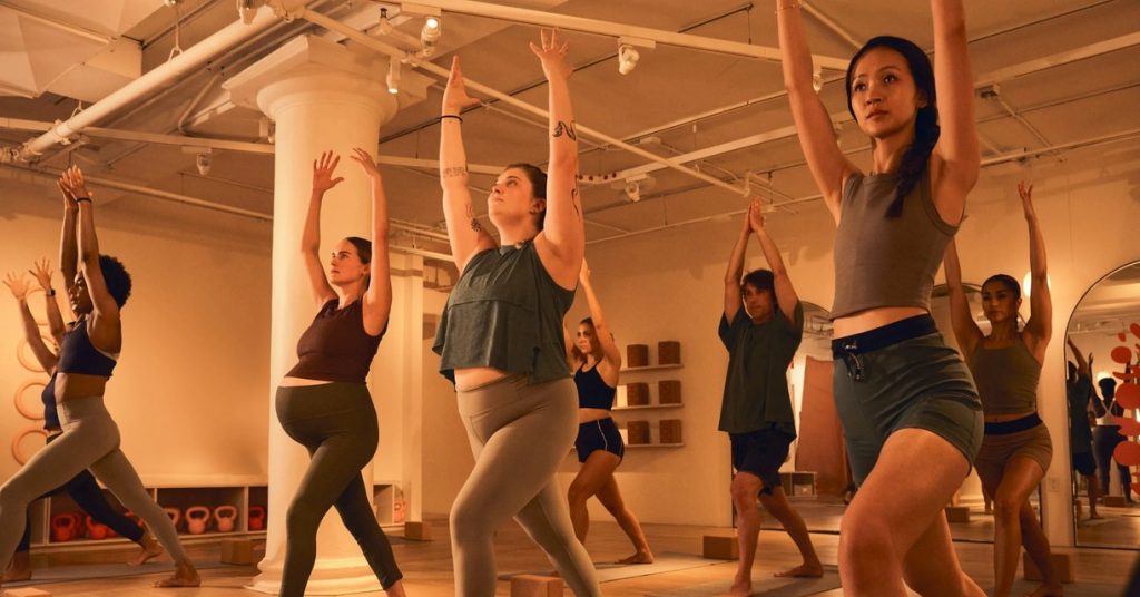 A yoga class in a sunlit studio, students reaching their arms overhead in a lunge