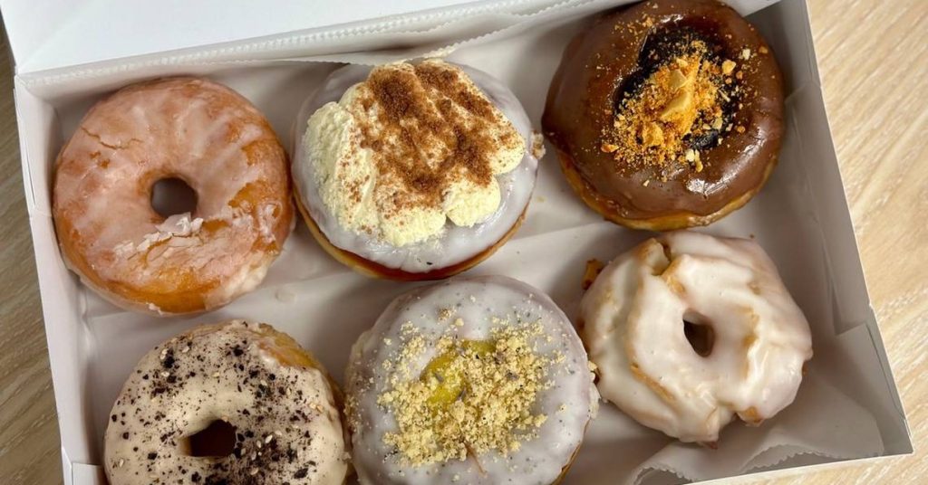 An open box of six assorted glazed and topped donuts, the kind of bakery surplus sold through the Goodie Bag app