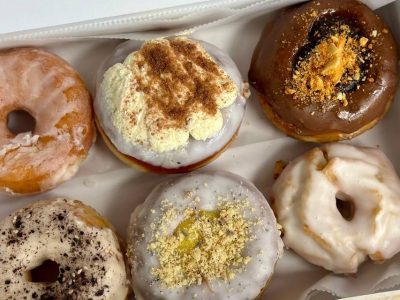 An open box of six assorted glazed and topped donuts, the kind of bakery surplus sold through the Goodie Bag app