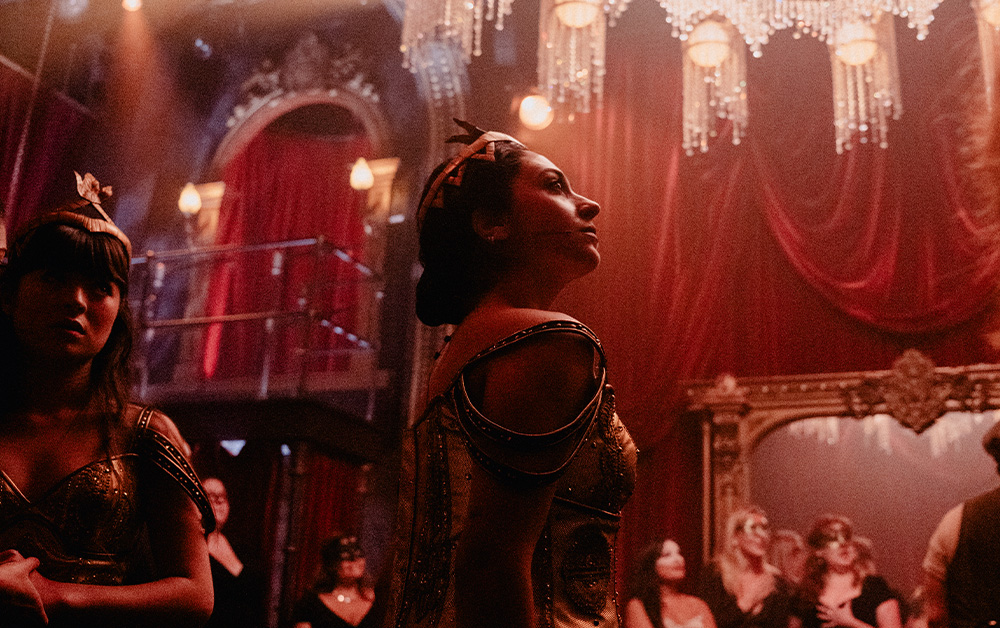 Performers in gold costumes at the masked ball in Masquerade, with masked audience members close behind them