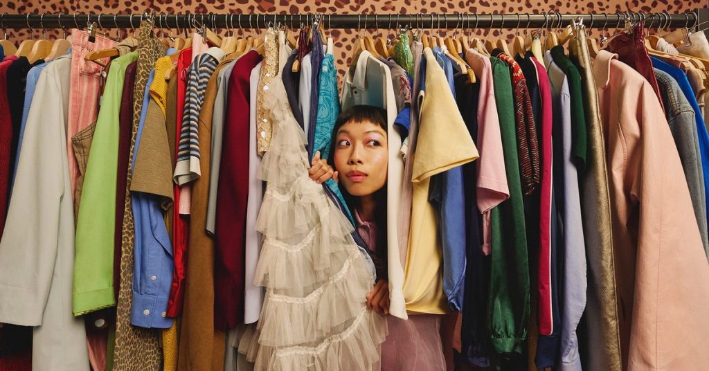 Racks of colorful secondhand clothes with a woman peeking out between the hangers