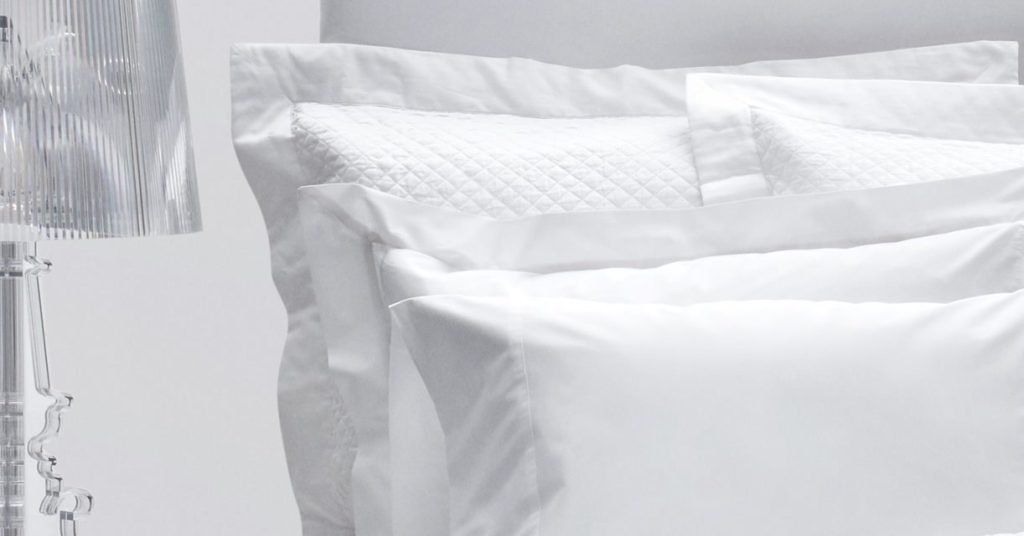 Prossioni white percale shams and pillowcases stacked against a headboard