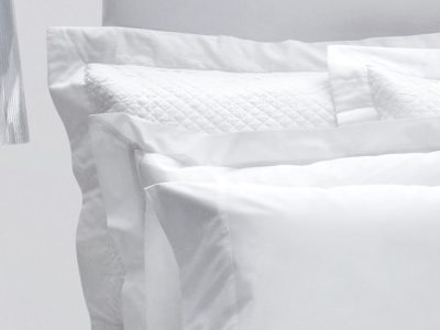 Prossioni white percale shams and pillowcases stacked against a headboard