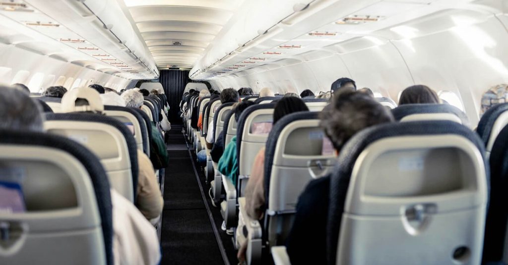 Passengers seated in the cabin of a commercial airplane, looking down the aisle