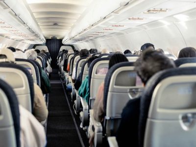 Passengers seated in the cabin of a commercial airplane, looking down the aisle